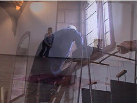 Two figures in a room with large windows